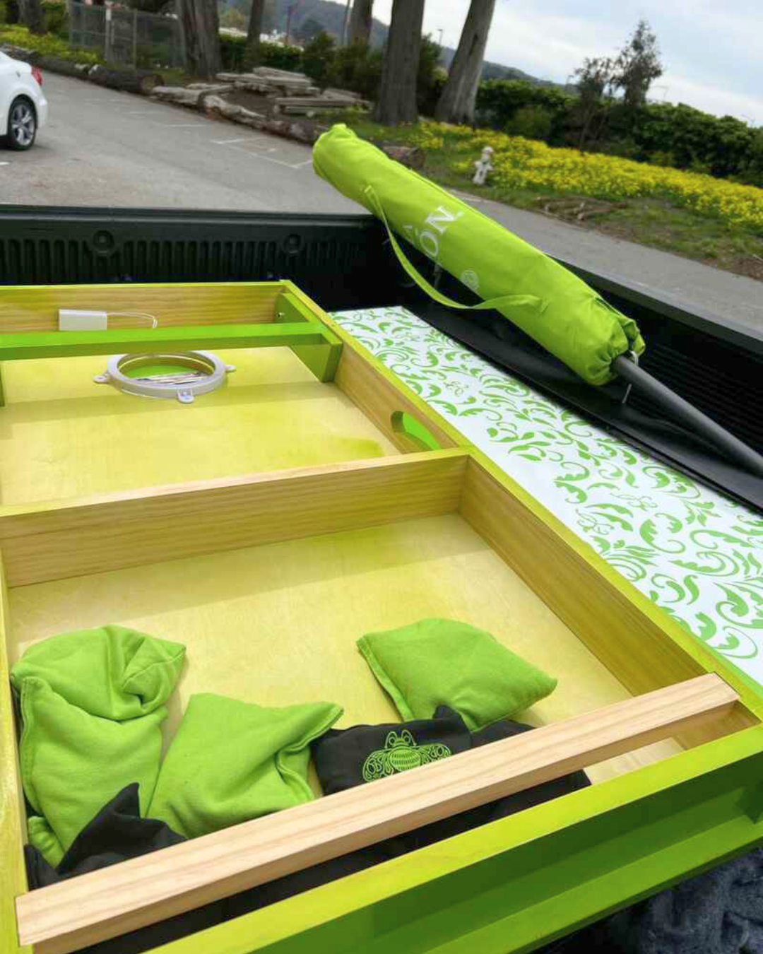 Bright green cornhole game board and bean bags packed in a delivery truck for summer event setup.