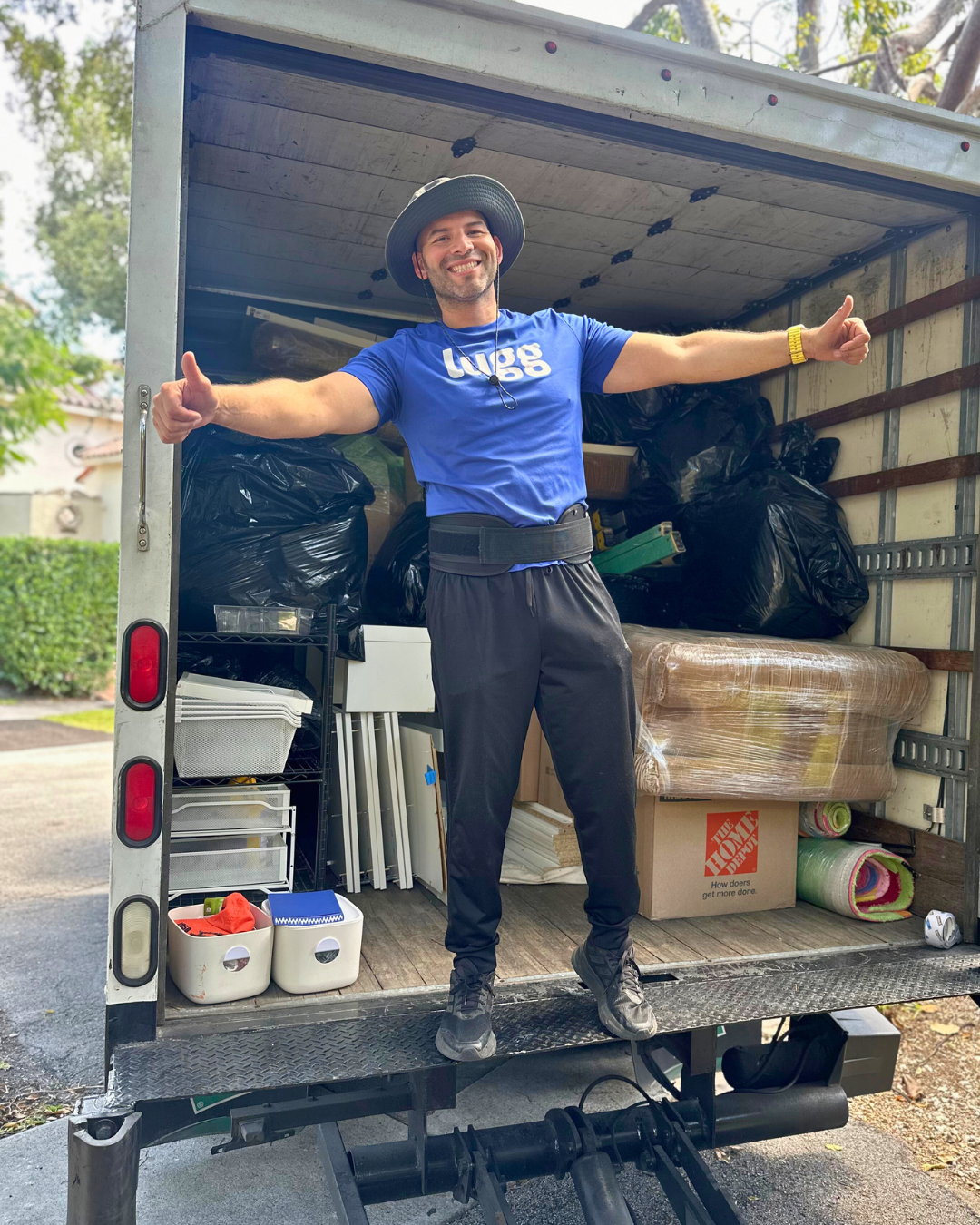A smiling Lugger in a blue Lugg shirt stands inside a moving truck filled with organized household items and furniture, posing with thumbs up after completing a Marketplace pickup.