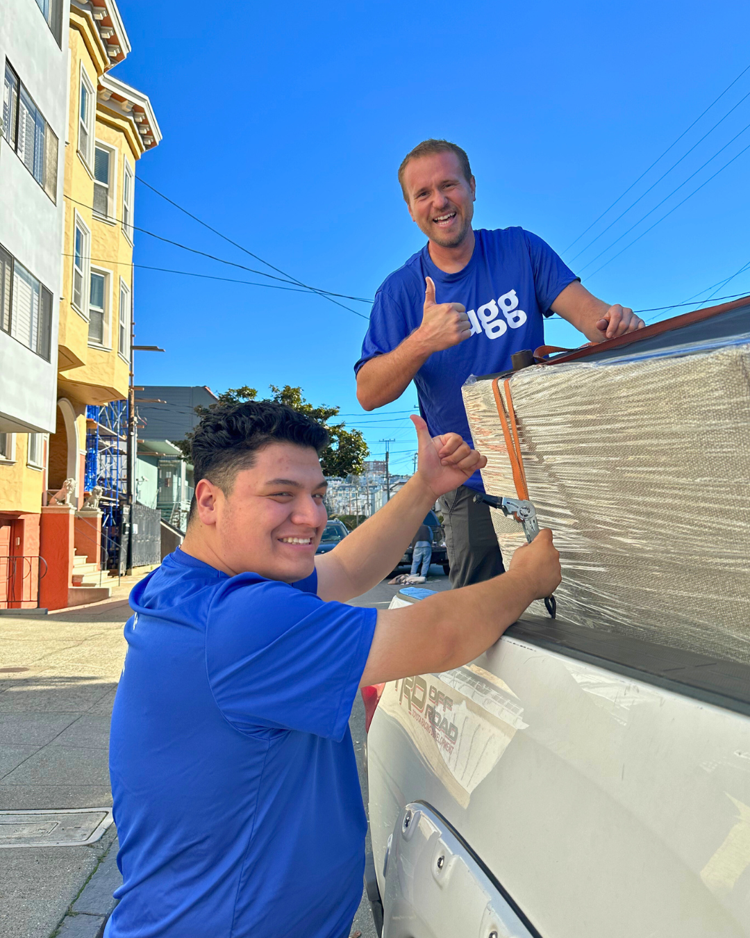 Two Luggers smiling and securing furniture with tie-down straps, showing job flexibility and teamwork.