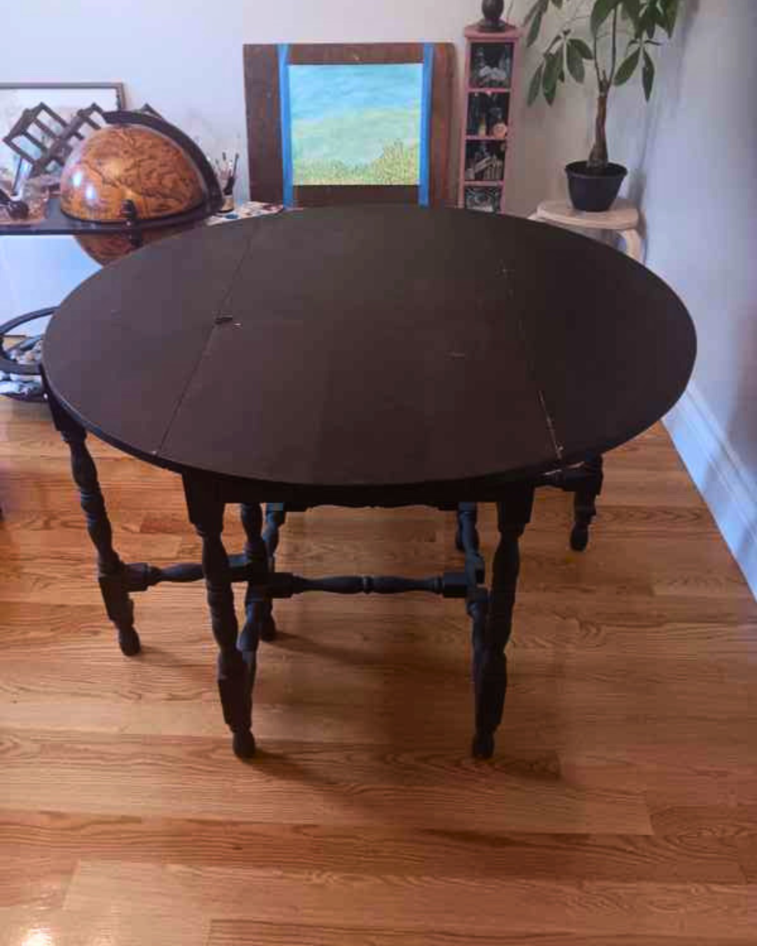 Dark wood round drop-leaf table with spindle legs displayed indoors on hardwood floor.