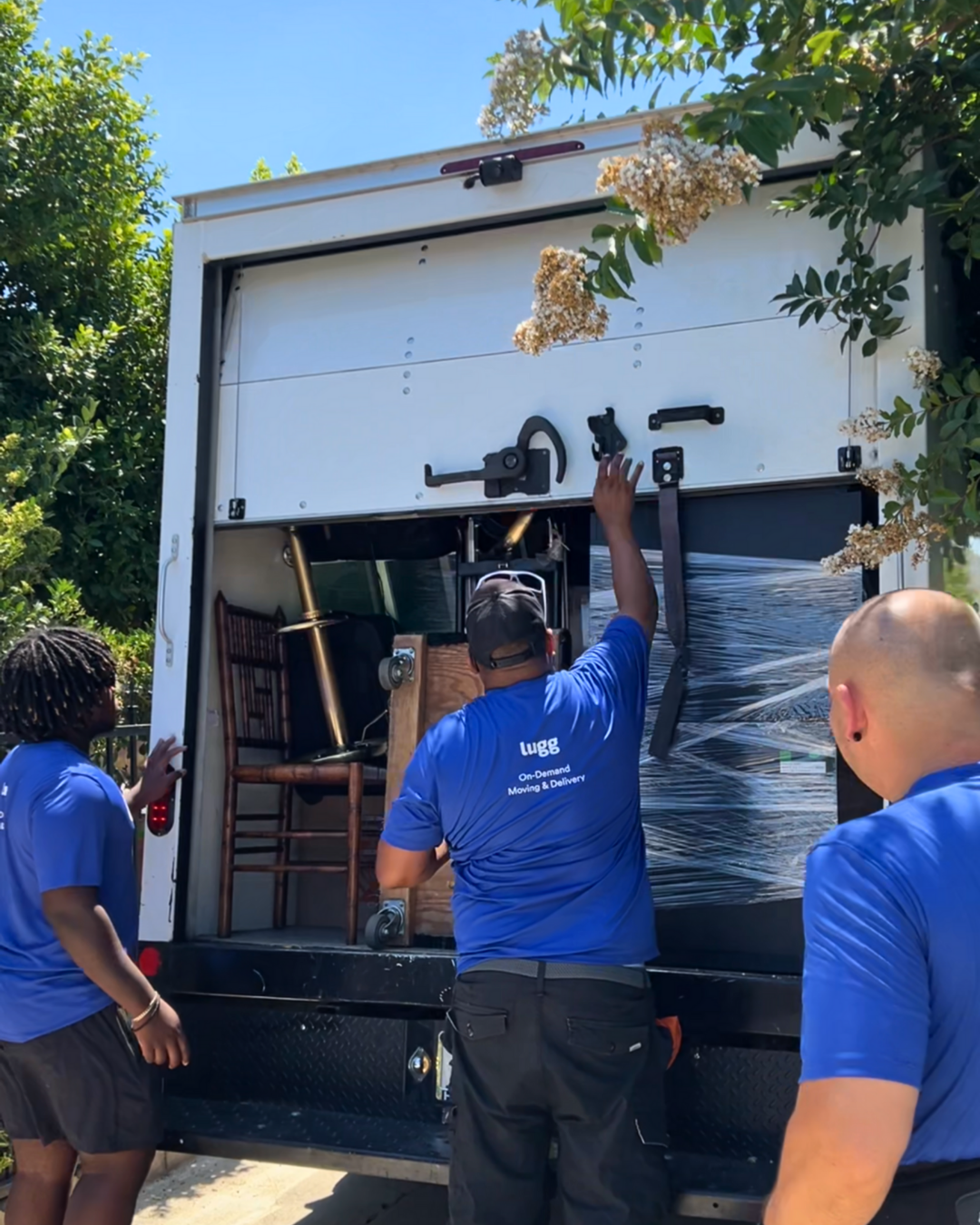 Lugg movers opening the back of a moving truck filled with furniture and wrapped items.