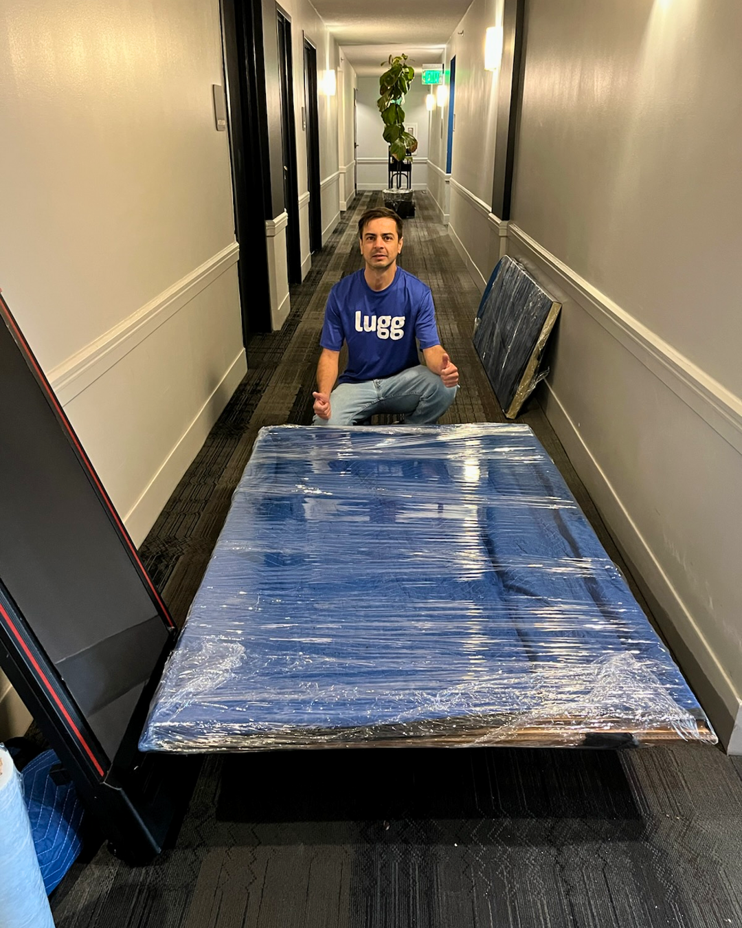 A Lugg mover kneeling in a hallway with a large mirror wrapped in moving blankets.