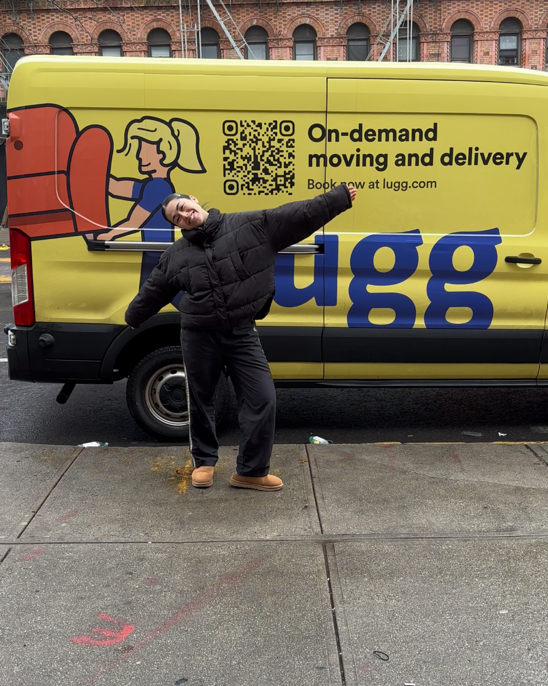 Smiling customer standing with arms outstretched in front of a yellow Lugg on-demand moving van in NYC.