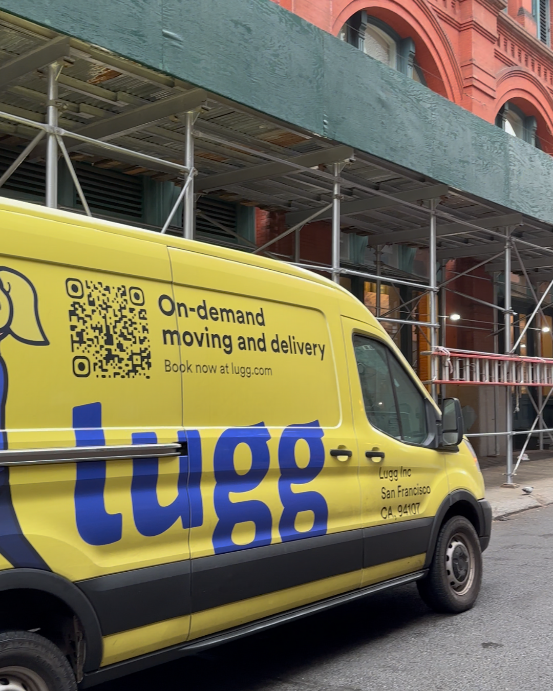 Yellow Lugg van parked along a NYC block with scaffolding overhead.