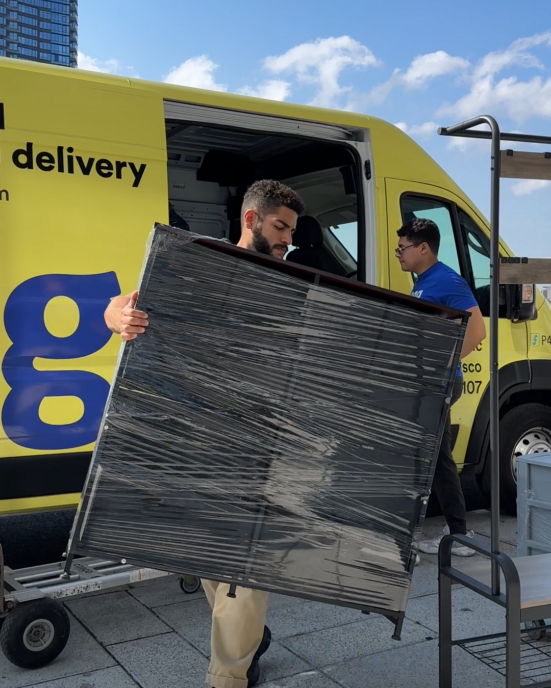 Two Lugg movers unloading a wrapped piece of furniture from a yellow Lugg van during a same-day move in NYC.