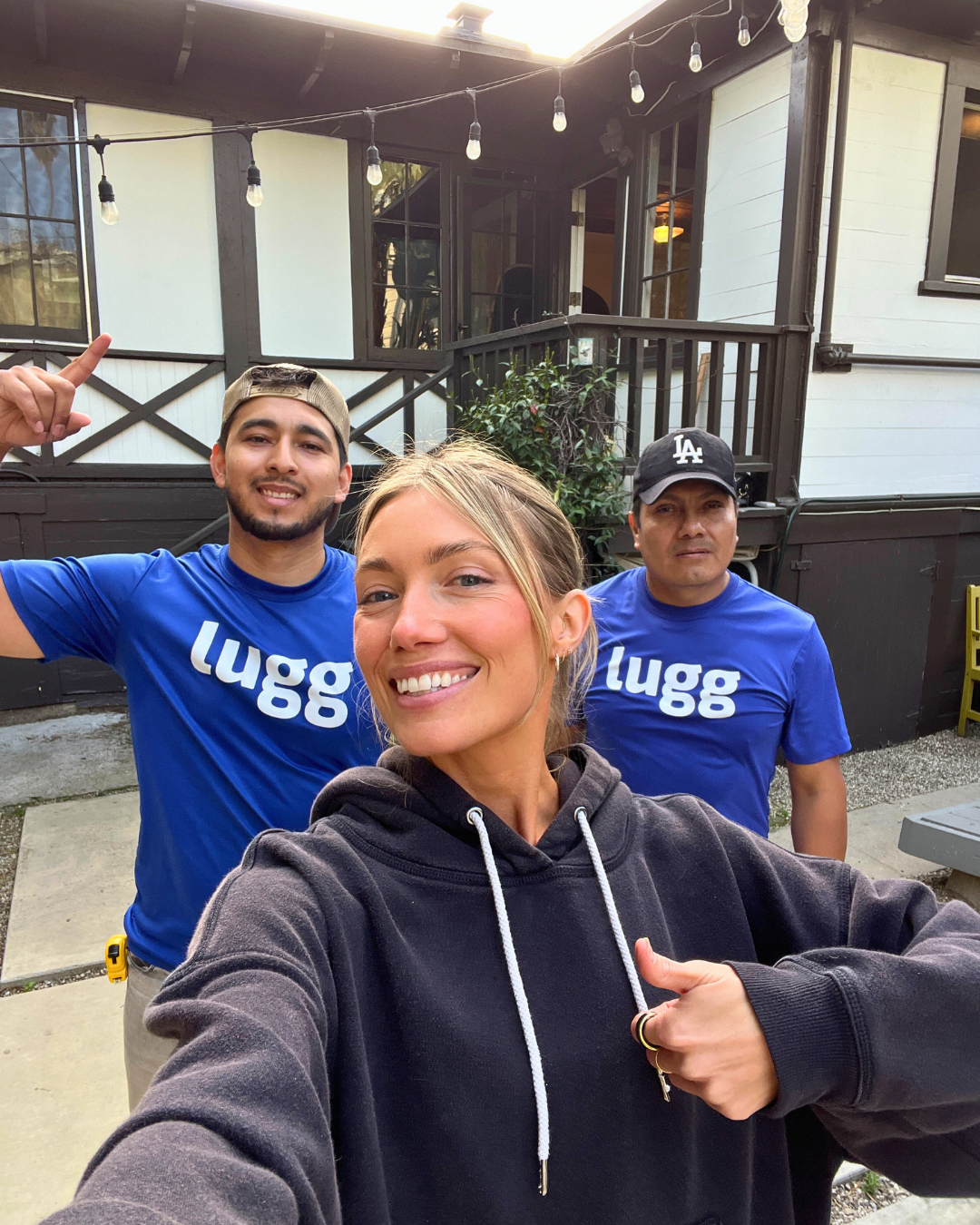 A customer smiling and taking a selfie with two Lugg movers in front of a house.