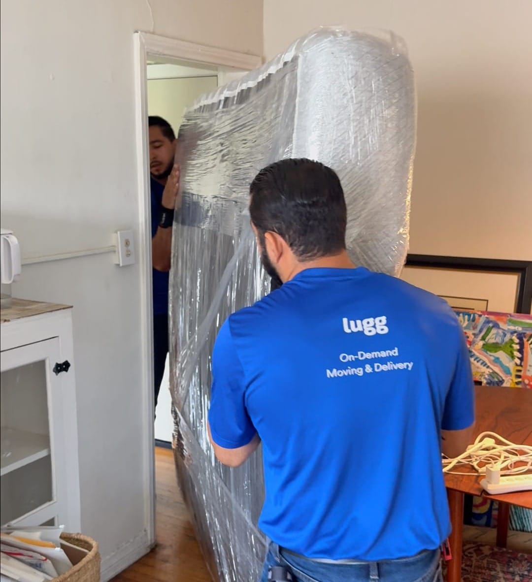 Two Lugg movers guiding a wrapped mattress through a tight doorway during removal.