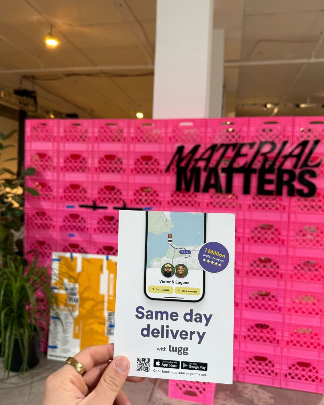 Lugg same-day delivery flyer held in front of the Material Matters NYC pink crate wall display