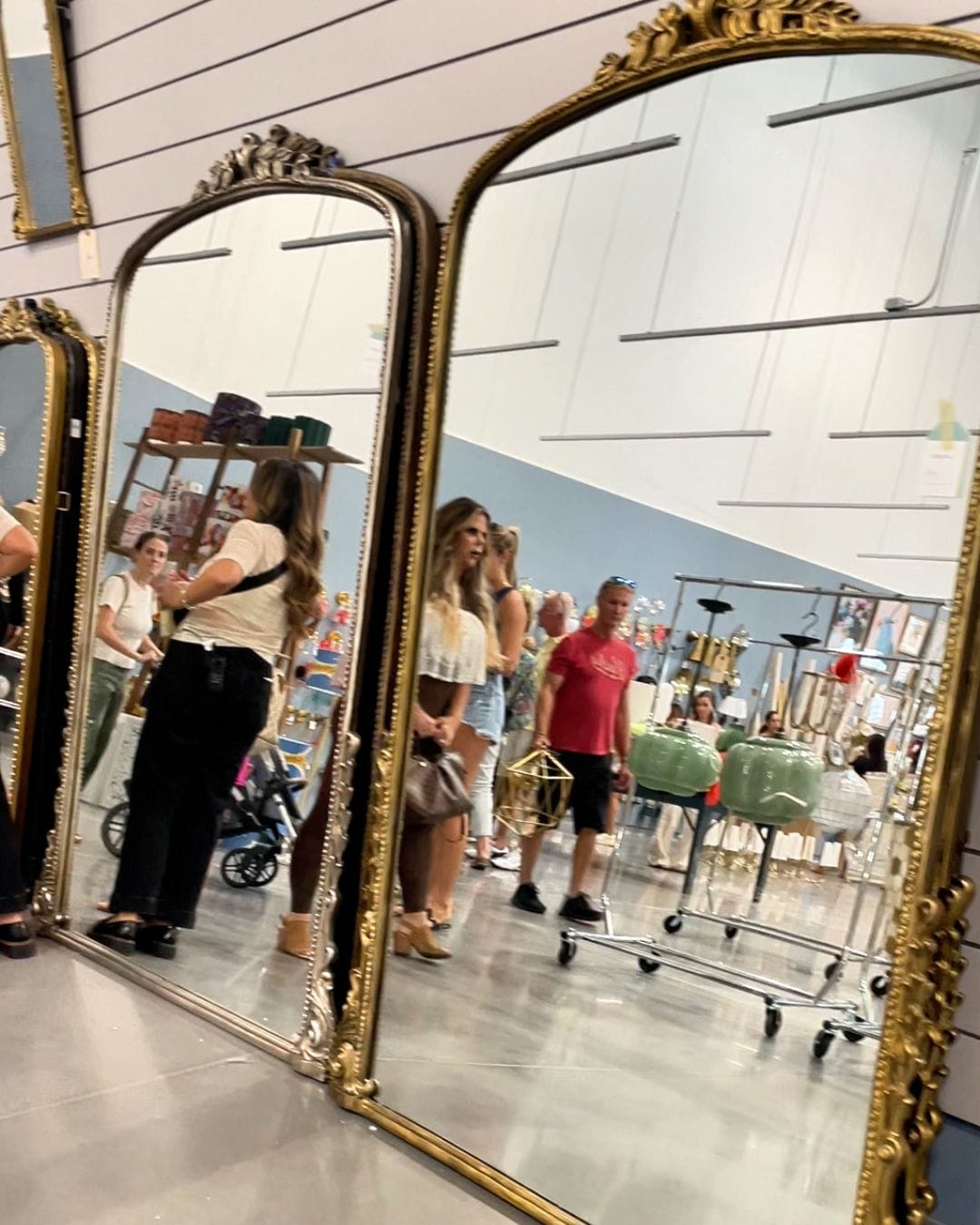 Gold-framed Gleaming Primrose mirrors on display at the Anthropologie Home Outlet with shoppers browsing in the background