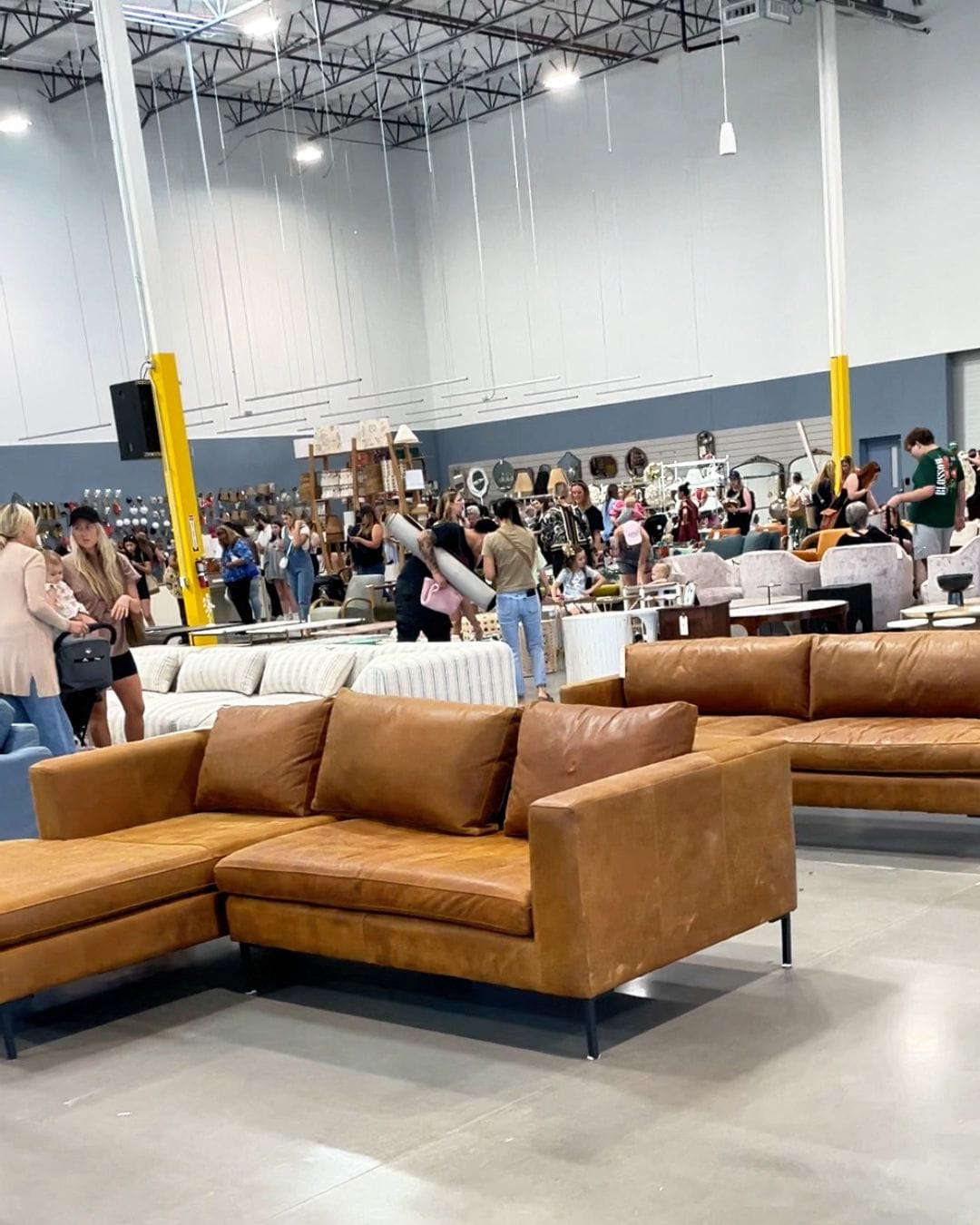 Shoppers browsing a camel leather sectional sofa during a busy sale day at the Anthropologie Home Outlet
