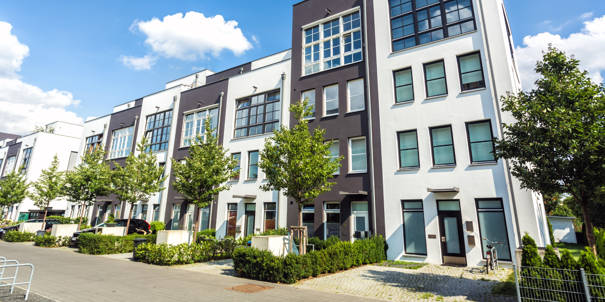 Front view of a modern apartment complex with trees and sidewalk