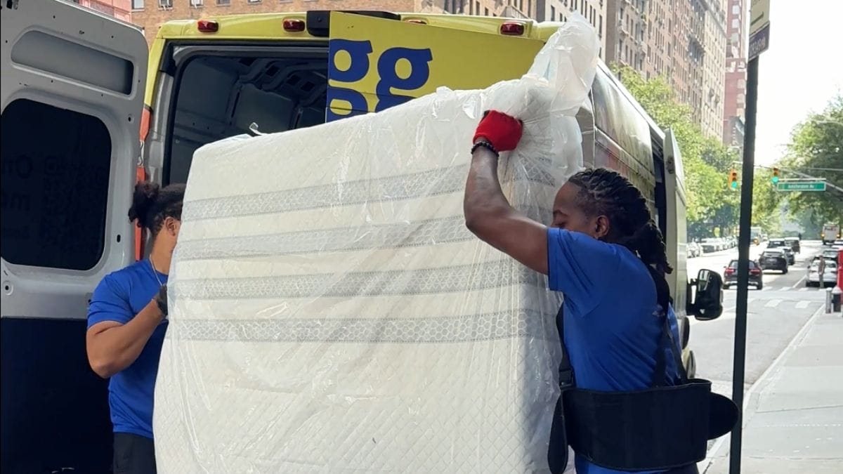 Two Lugg movers loading a wrapped mattress at the curb for removal and disposal.